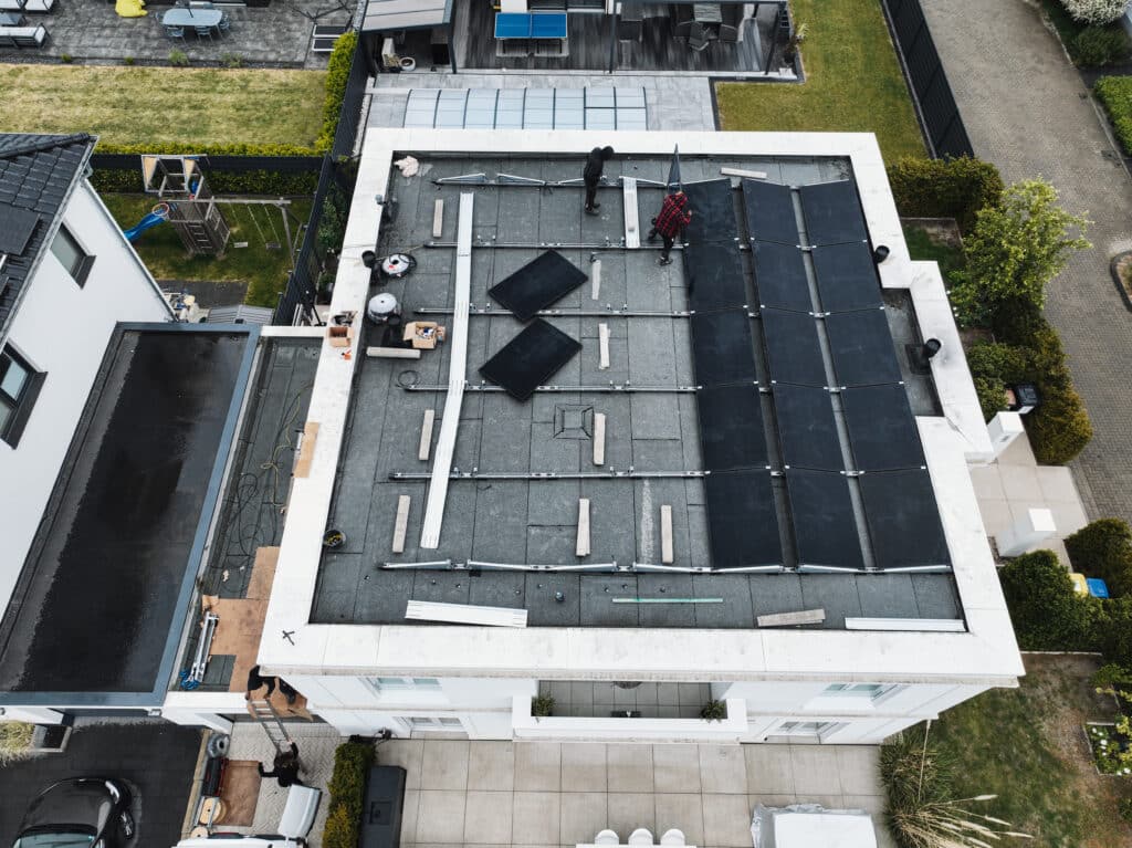 alt="Moderne Photovoltaikanlage auf Flachdach in der Aufbauphase mit sichtbaren Montageschienen und installierten Solarmodulen."